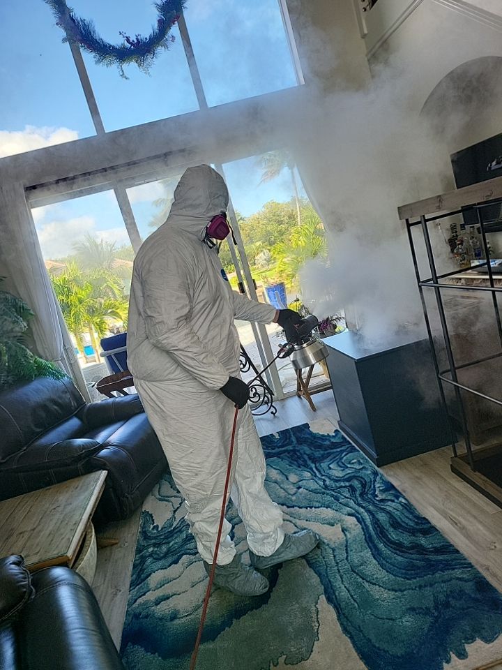 Technician in full PPE thermal fogging open-concept living room with pool view